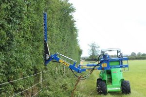 Slanetrac MB900 MultiBoom Carrier fitted with an HC180L hydraulic hedge trimmer on a compact loader, trimming roadside hedges and overgrown vegetation with precision.