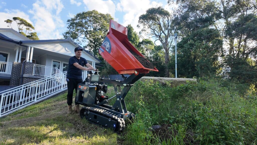 Slanetrac HT1000 mini site dumper tipping dirt out on a worksite. The operator has raised the tipping bin and is pouring dirt out onto the ground.